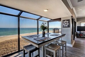 A dining area with a view of the beach, a potted plant, and a television in the corner. - Penthouse @ The Cabana-Overlooking CB Boardwalk (Carolina Beach)