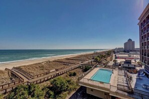 Un hotel frente a la playa con piscina, pasarelas de madera y vistas al océano.