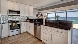 Cozinha moderna com armários brancos, eletrodomésticos de aço inoxidável e uma grande janela com vista para o oceano.