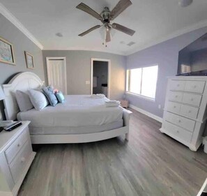 Un dormitorio con cama, mesitas de noche, cómoda, ventilador de techo y ventana.