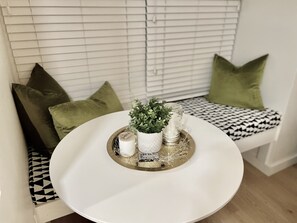 A round white table with a tray of decorative items, including a small plant, candles, and a glass jar, placed on a bench with patterned cushions.