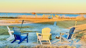 A beach scene with three Adirondack chairs and a wooden dock extending into a body of water.