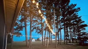 A covered outdoor area with string lights, trees, and a grassy field.