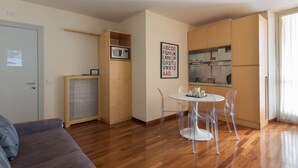 Un espace de vie compact comprenant un coin cuisine, un coin repas avec une table ronde et des chaises, un canapé et un meuble avec un four à micro-ondes.