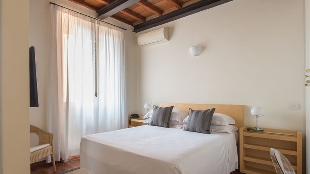 Une chambre à coucher avec un lit, des tables de chevet, une lampe, une chaise et une fenêtre avec des rideaux.