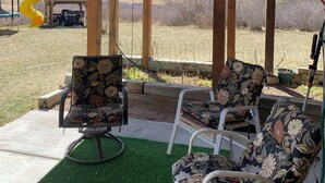 Un patio couvert avec deux chaises et une petite table, un toboggan jaune et une vue sur un paysage rural.