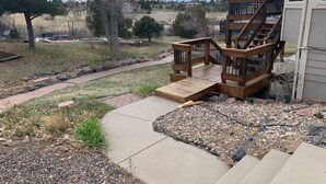 Une terrasse en bois avec une rampe menant à une maison, le tout entouré d’un jardin aménagé avec du gravier et de petites plantes.