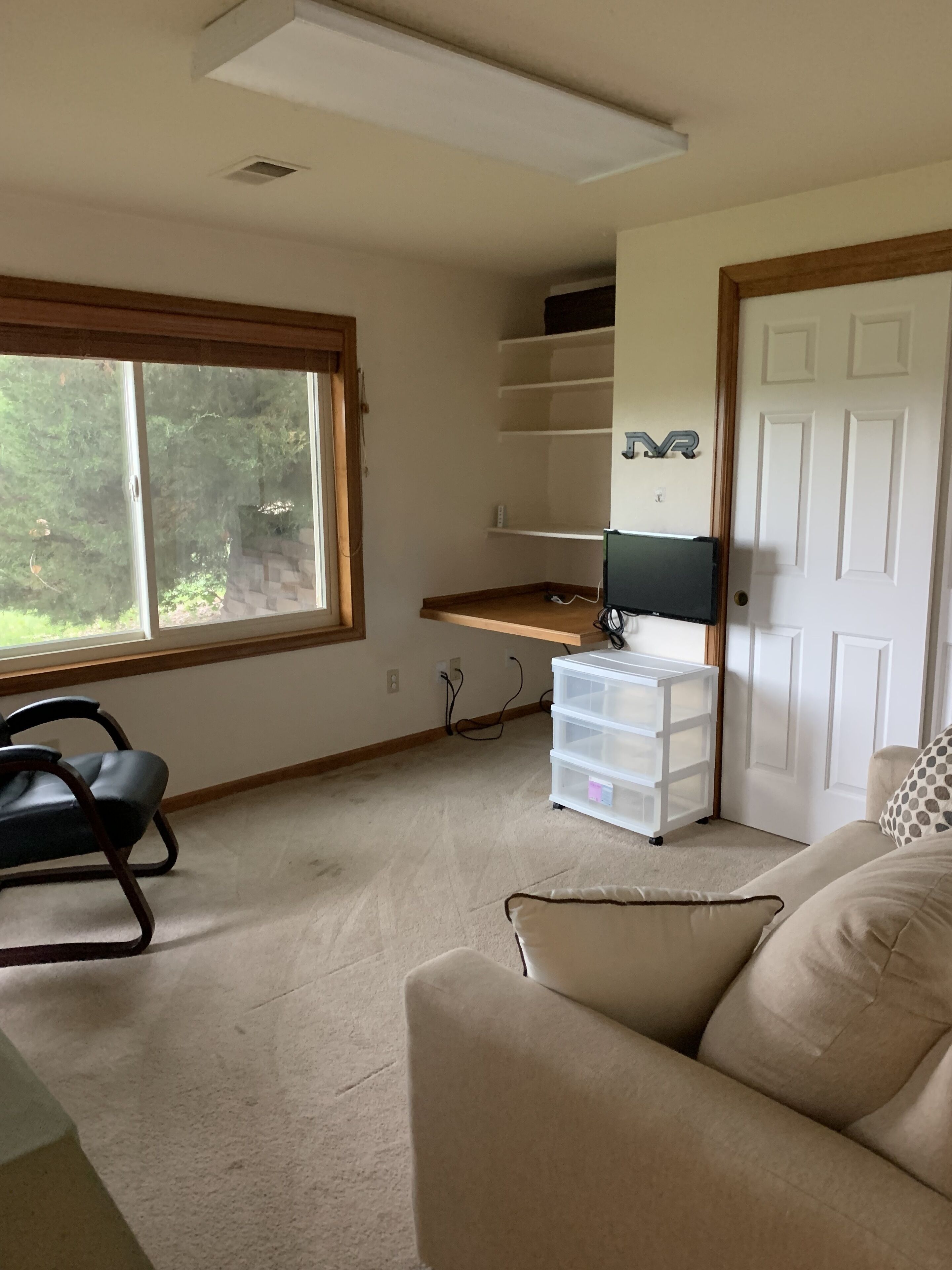 A room with a large window, a desk with a computer, a chair, and a storage unit.