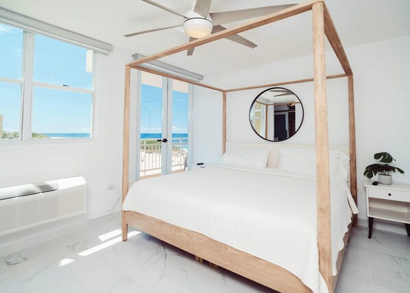 A spacious bedroom with a large bed, a ceiling fan, a round mirror, and a view of the ocean through large windows. - #20 Luxury True Oceanfront Designer Penthouse (Isabela)
