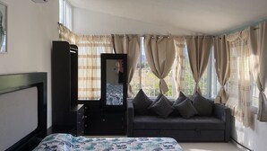 Un dormitori amb un llit, una petita taula de nit, un mirall, un sofà i una finestra amb cortines.