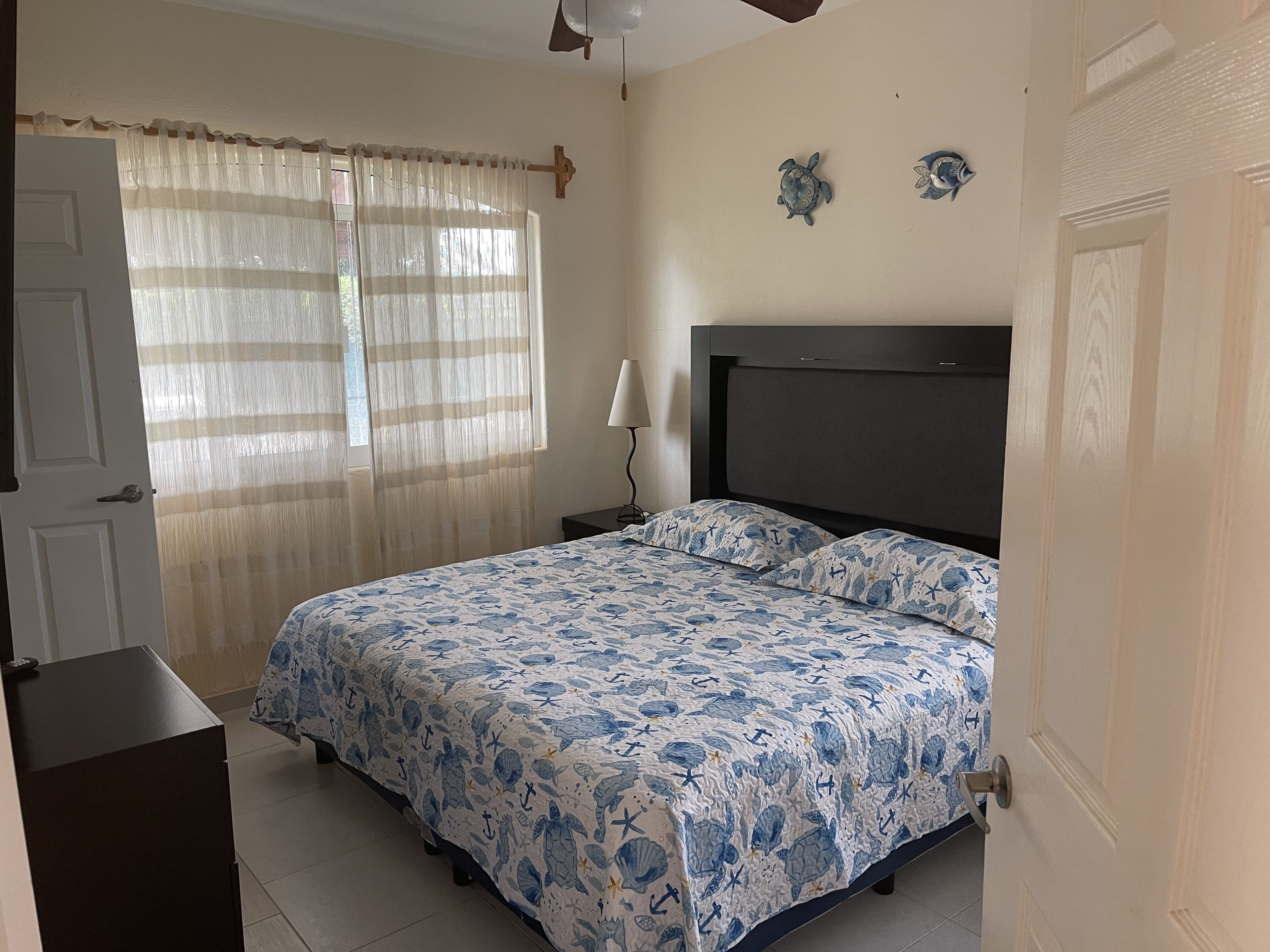 A bedroom with a bed, a nightstand, a lamp, and a window with curtains.