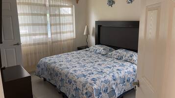 A bedroom with a bed, a nightstand, a lamp, and a window with curtains.
