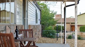 A covered patio with a table and chairs, a stone wall, and a view of a building in the background. - Casa Little Bird (Los Alamos)