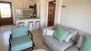 A spacious living area with a sofa, a round coffee table, and a kitchen in the background. - 2 BR flat overlooking open lagoon and private pool (Red Sea Governorate)