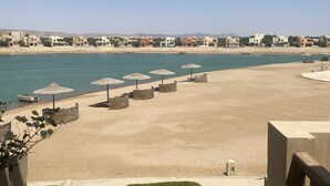 A beach view with a clear sky, a sandy beach, and a row of umbrellas. - 2 BR flat overlooking open lagoon and private pool (Red Sea Governorate)