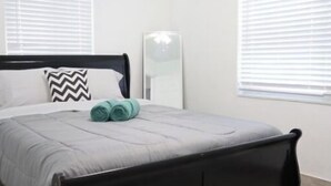 Ein Schlafzimmer mit einem Bett, einem Spiegel und zwei Fenstern mit Jalousien.