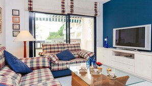 Ein Wohnzimmer mit einer Sofagarnitur, einem Glastisch, einem Fernseher und Blick ins Freie.