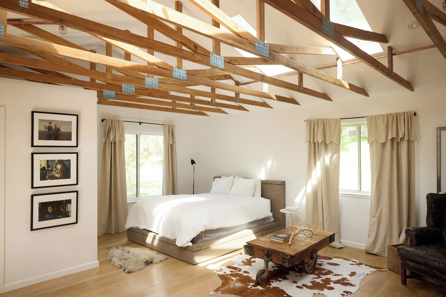 A bedroom with a bed, a wooden ceiling, a cowhide rug, and a leather armchair.