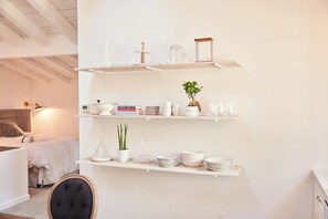 A room with a bed, a chair, and three white shelves with various items.