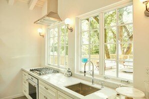 A kitchen with a large window, a stove, and a sink.