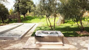 Uma banheira de hidromassagem em um jardim com deck de madeira e um pátio de concreto.