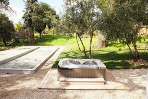 Uma banheira de hidromassagem em um jardim com deck de madeira e um pátio de concreto.