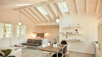 Um interior moderno com teto estilo loft, área de jantar com mesa de madeira e prateleiras embutidas com utensílios de cozinha.