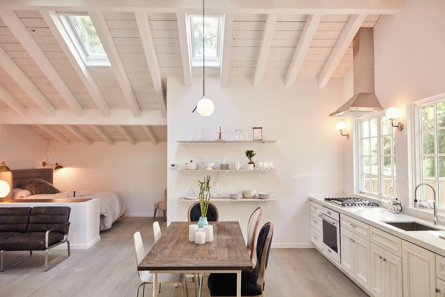 A modern kitchen with white cabinetry, a wooden dining table, and pendant lighting.
