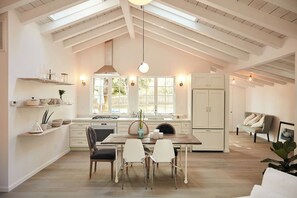 A modern kitchen with a dining area, featuring a skylight, wooden beams, and a view of the outdoors.