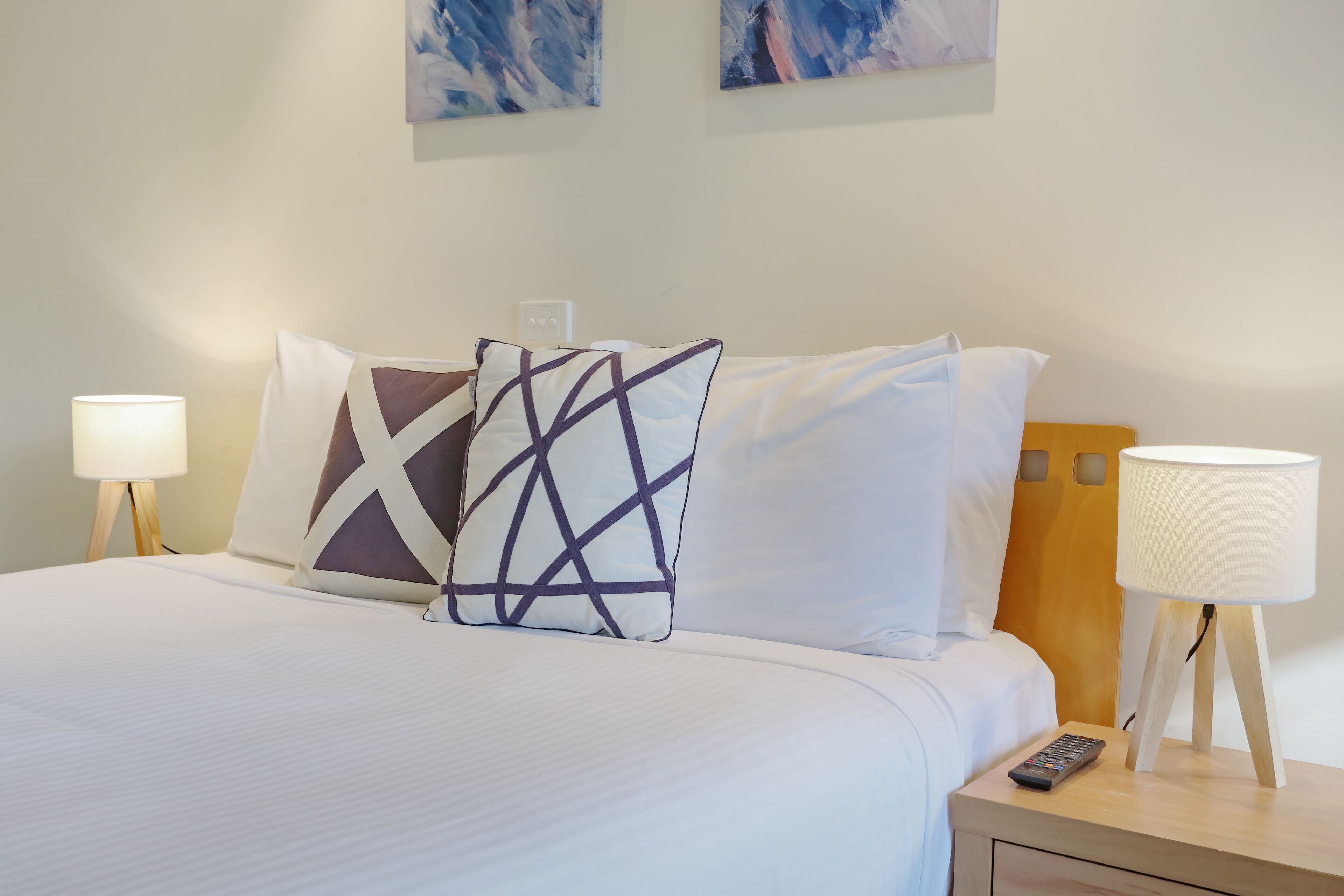 A neatly made bed with white linens and two decorative pillows, flanked by bedside lamps on wooden nightstands.