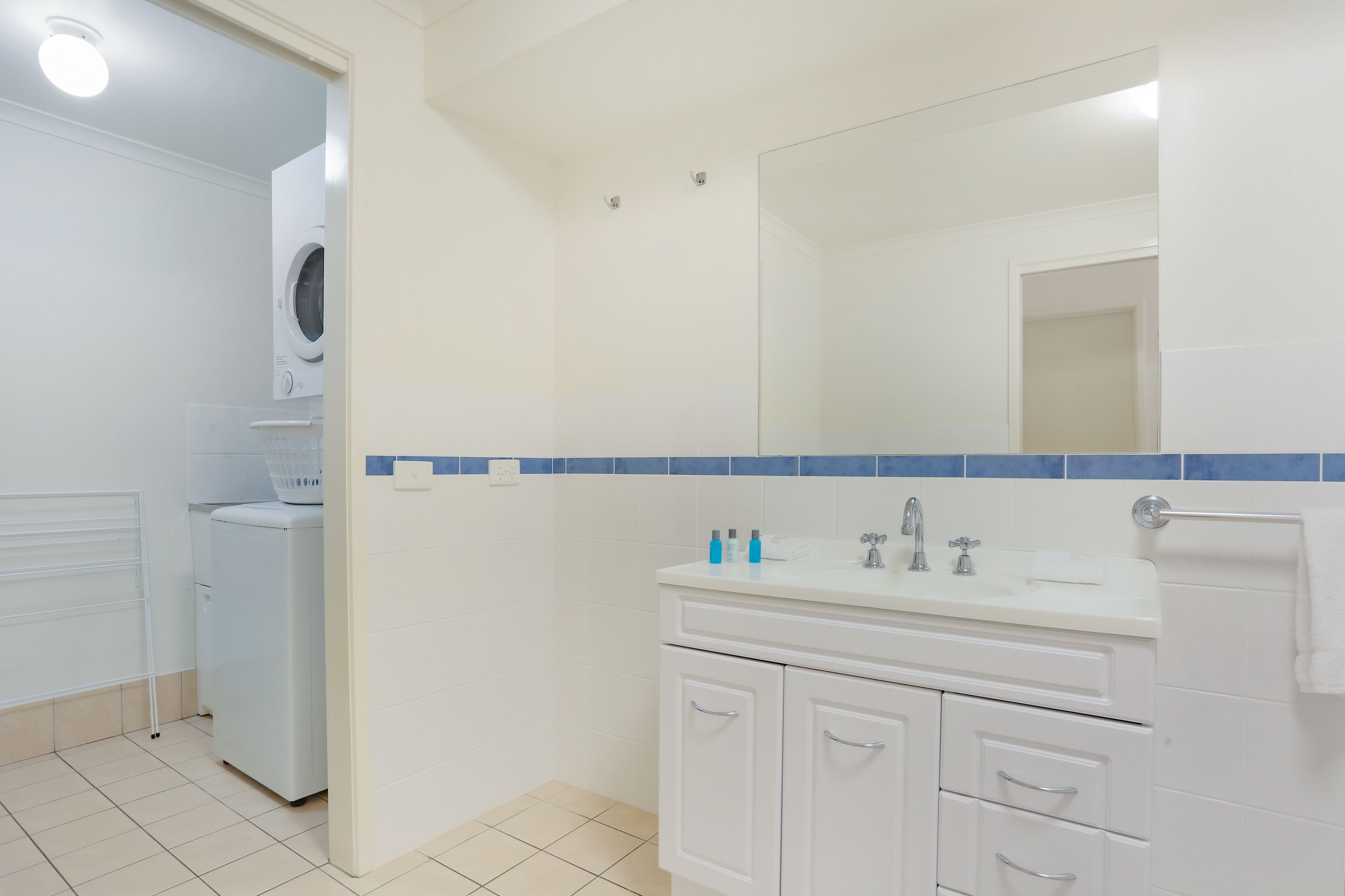 A bathroom with a white sink, mirror, and cabinets, a washing machine, and a towel rack.
