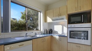 A modern kitchen with wooden cabinets, a dishwasher, a microwave, and an oven. - Sorrento Apartments Merimbula (Merimbula)