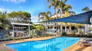 A swimming pool with lounge chairs, a shaded area, and a fenced garden. - Sorrento Apartments Merimbula (Merimbula)