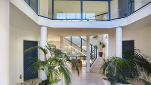 A spacious indoor area with a central staircase, potted plants, and a seating area. - Sorrento Apartments Merimbula (Merimbula)