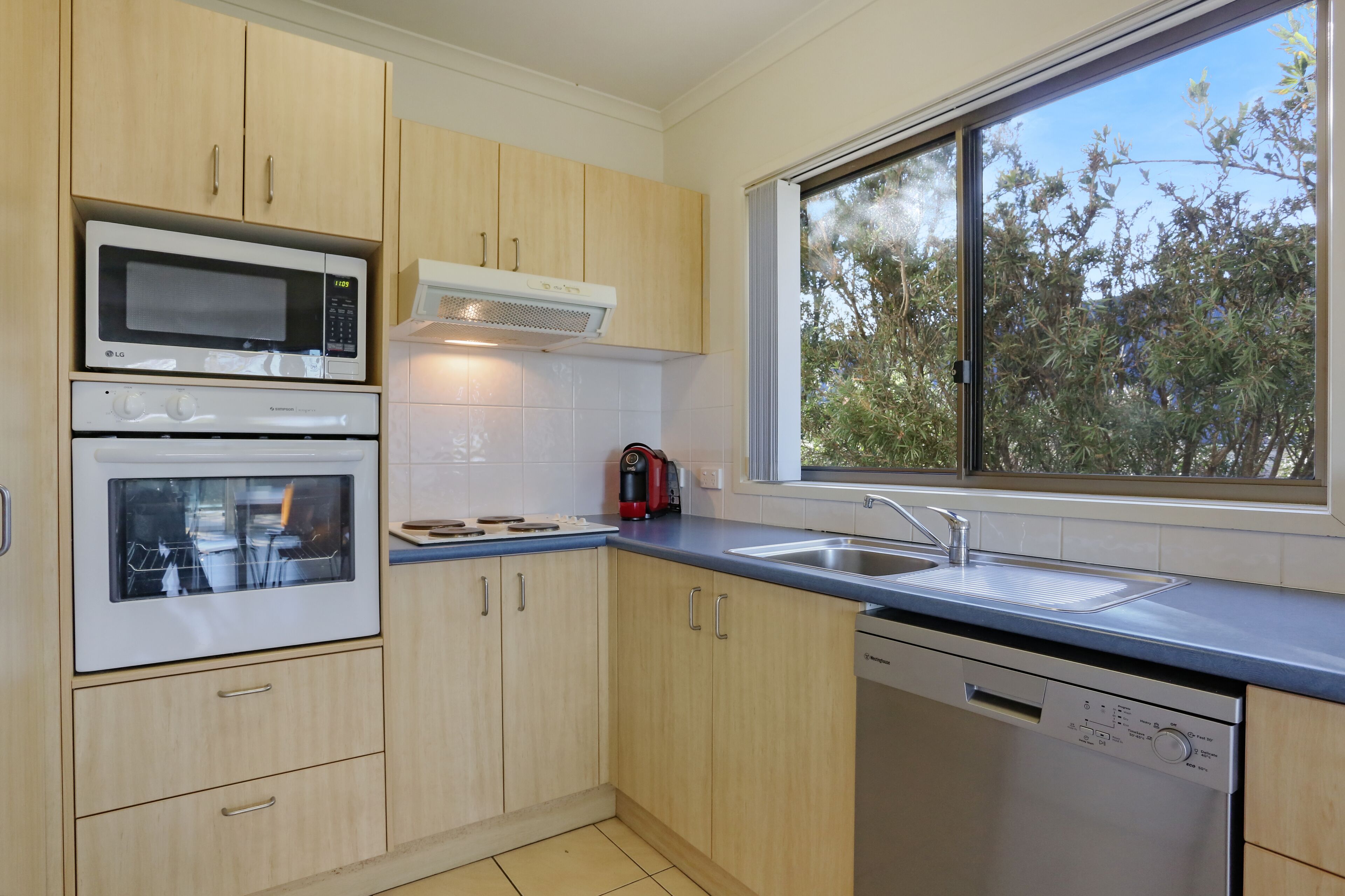 Uma cozinha moderna com eletrodomésticos embutidos, uma janela com vista para árvores e uma lava-louças.