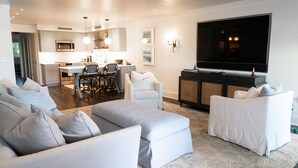 Una sala moderna con un sofá, dos sillones, una zona de comedor con mesa y sillas, una cocina con microondas y un televisor montado en la pared.