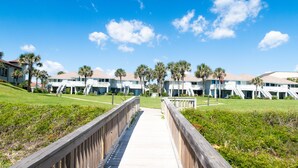 Un resort con varias edificaciones, un paseo marítimo de madera y palmeras.