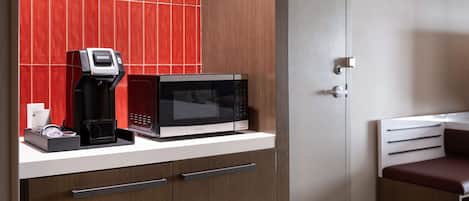 Una kitchenette compacta con microondas, cafetera y cajones para guardar objetos.