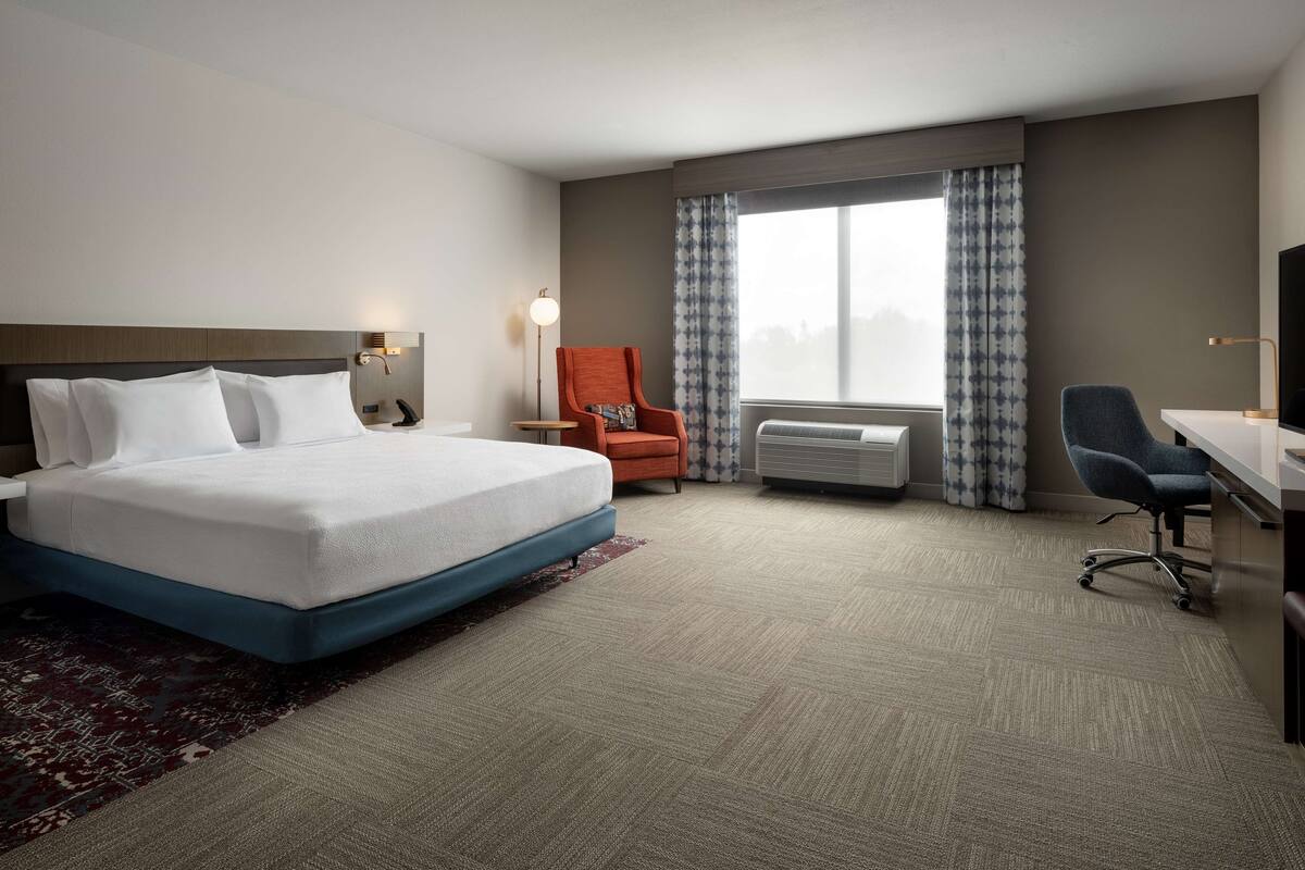A hotel room with a large bed, a desk, an orange chair, and a TV.