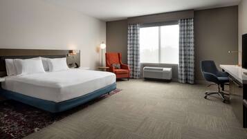 A hotel room with a large bed, a desk, an orange chair, and a TV.