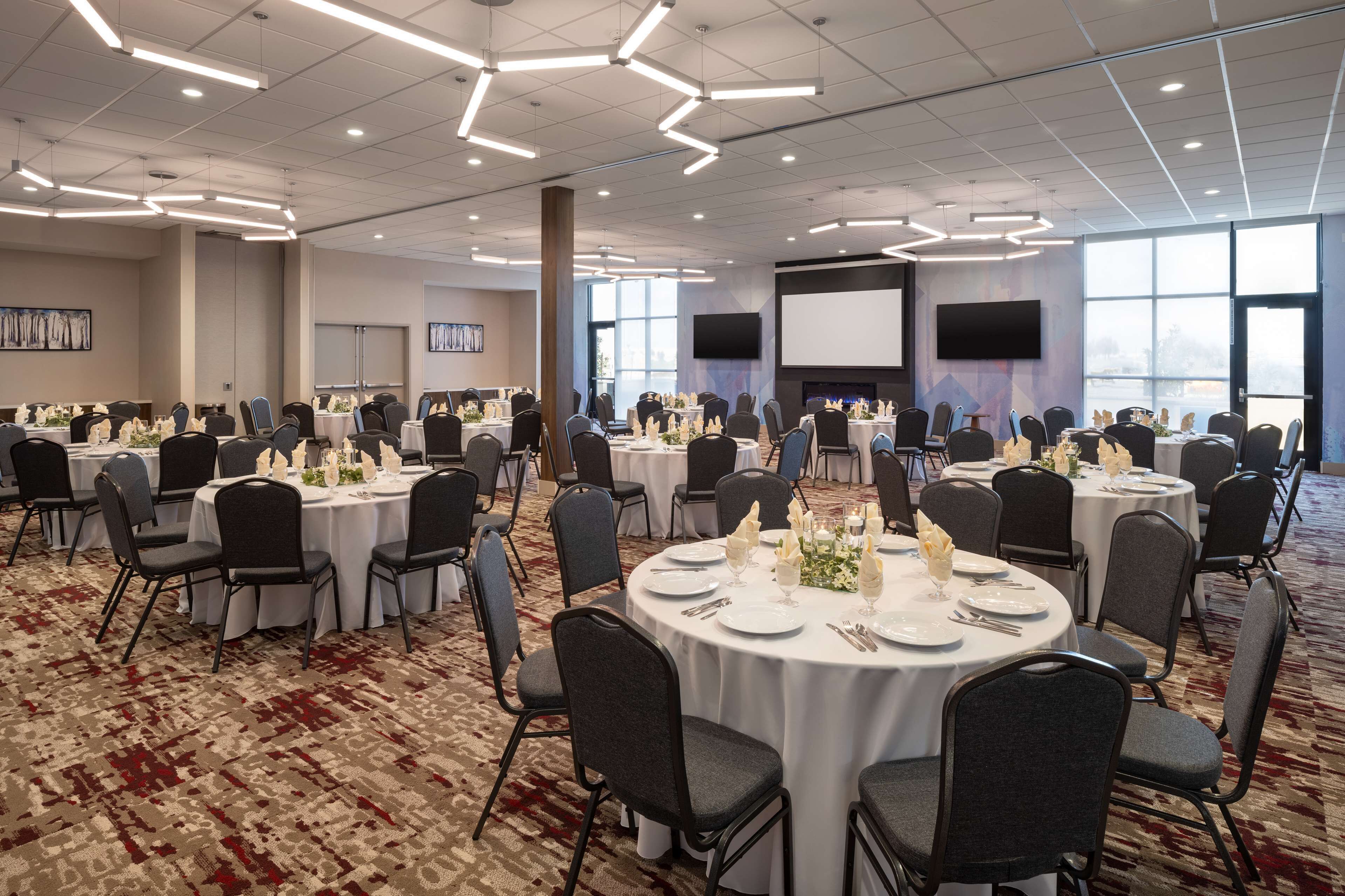 Un salón de conferencias con varias mesas redondas, cada una con mantel blanco, sillas y centros de mesa florales.