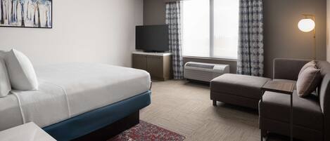 Una habitación de hotel con cama, sofá, televisor y ventana con cortinas.