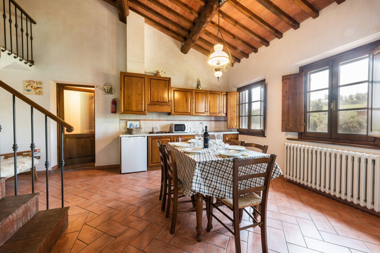 A kitchen with wooden cabinets, a dining table set for four, and a staircase leading to another level.