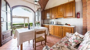 Une cuisine avec des meubles en bois, une table à manger avec des chaises et une vue sur l’extérieur, visible à travers une porte en arc de cercle.