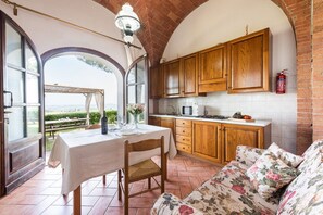 A kitchen with wooden cabinets, a dining table with chairs, and a view through an arched doorway.