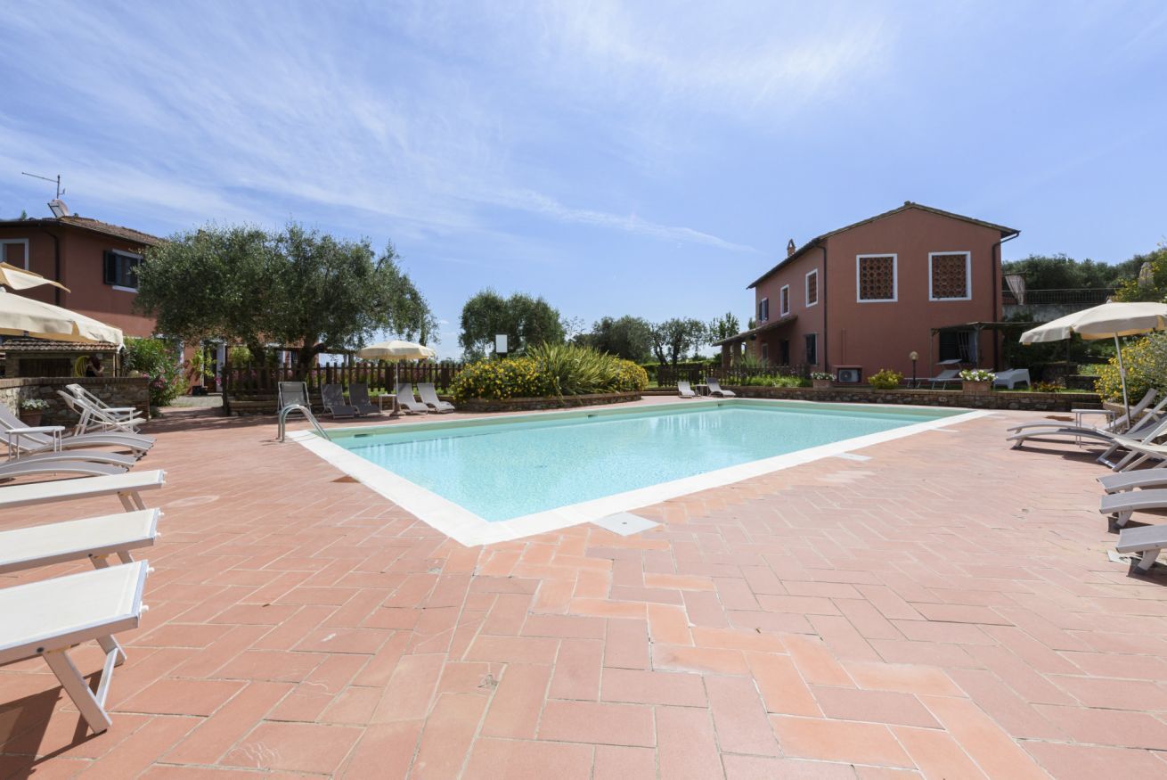 A swimming pool with lounge chairs, a brick patio, and two buildings with windows.
