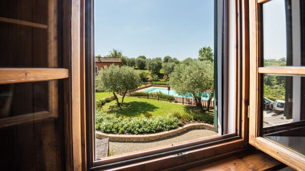 Une vue à travers une fenêtre sur un jardin aménagé, avec une piscine, des arbres et une clôture en bois.