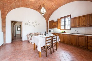 A kitchen with wooden cabinets, a dining table with chairs, and a brick ceiling.
