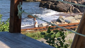 A wooden deck overlooking a rocky shoreline with a rope barrier. - AUBERGE ET SPA LE HUARD (Chandler)