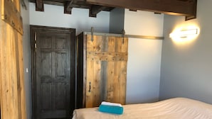 A bedroom with a wooden wardrobe, a bed with a white sheet, and a wall-mounted light fixture. - AUBERGE ET SPA LE HUARD (Chandler)